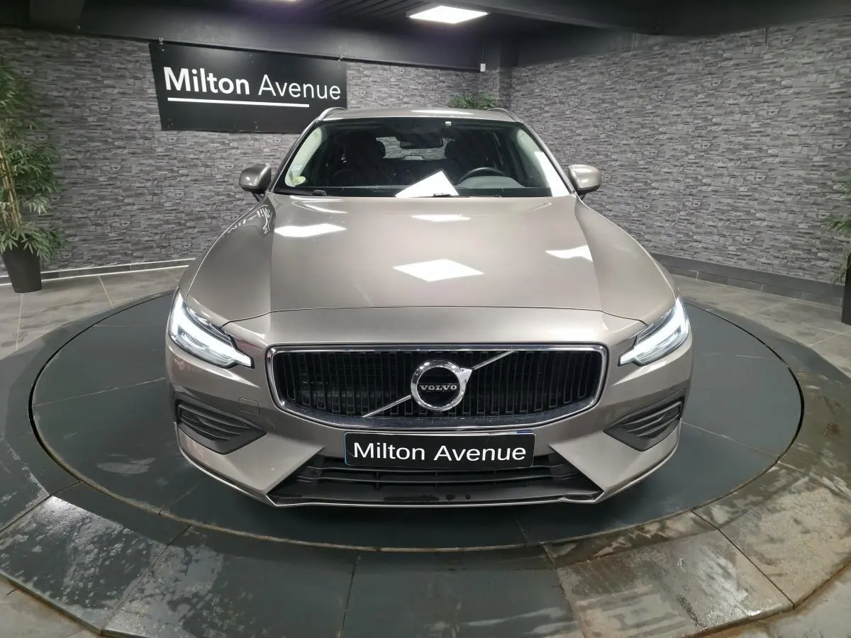 Vue frontale d'une Volvo V60 gris métallisé 2021 avec calandre chromée et phares LED allumés.