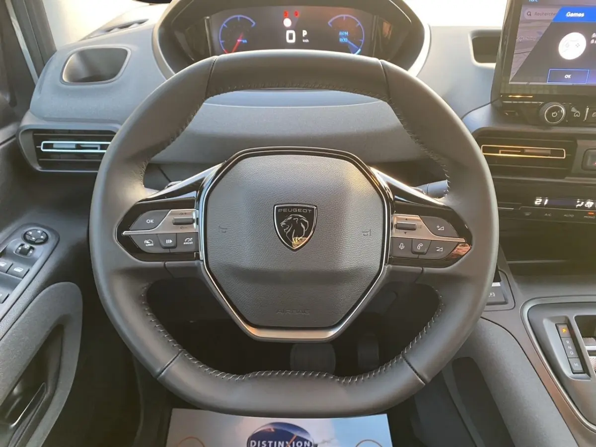 Vue rapprochée du volant cuir noir du Peugeot Rifter III Ph.2 avec commandes intégrées et tableau de bord digital.