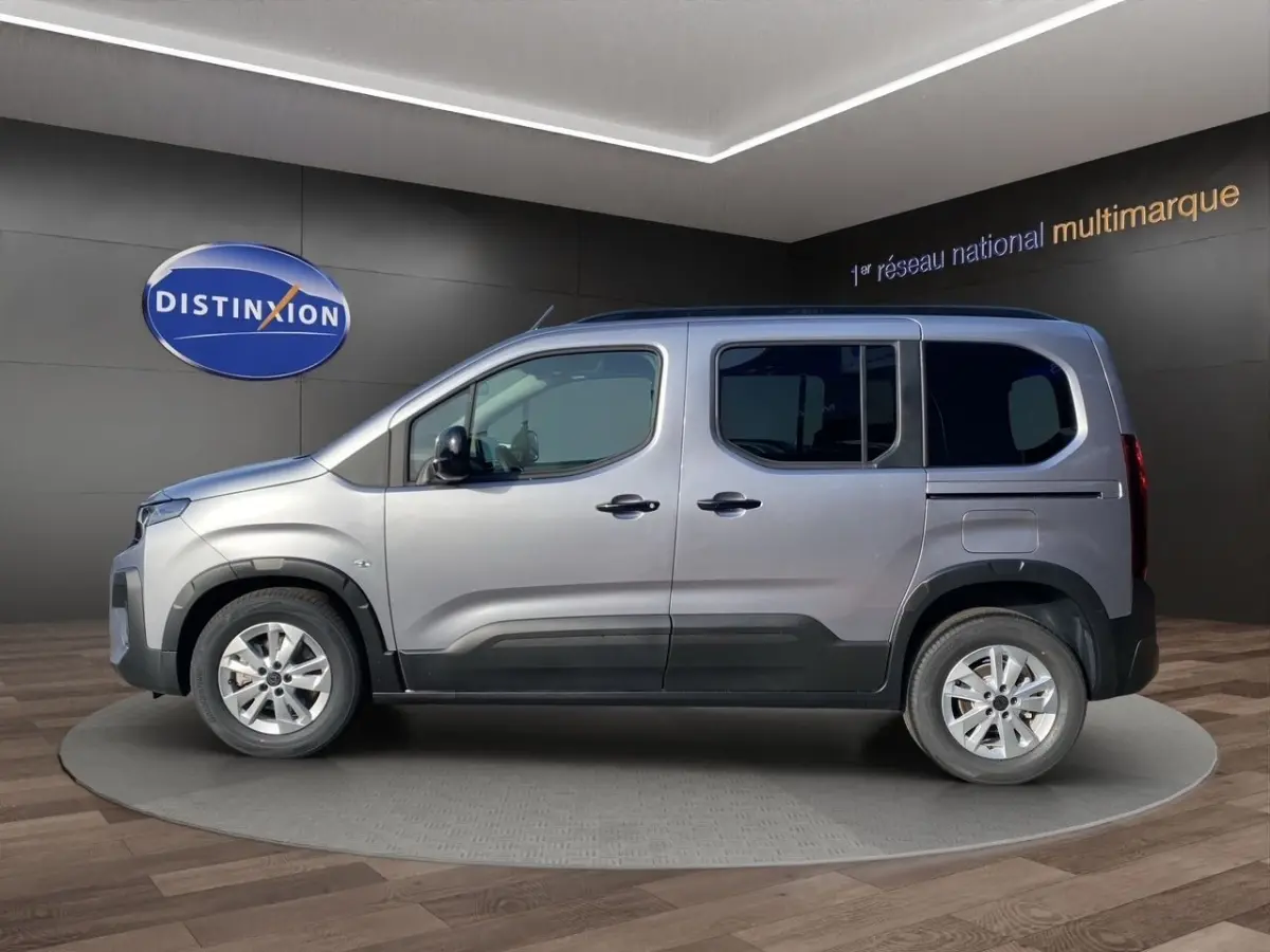 Profil droit d'un Peugeot Rifter gris clair 2026 en présentation showroom avec jantes alliage et protections noires.