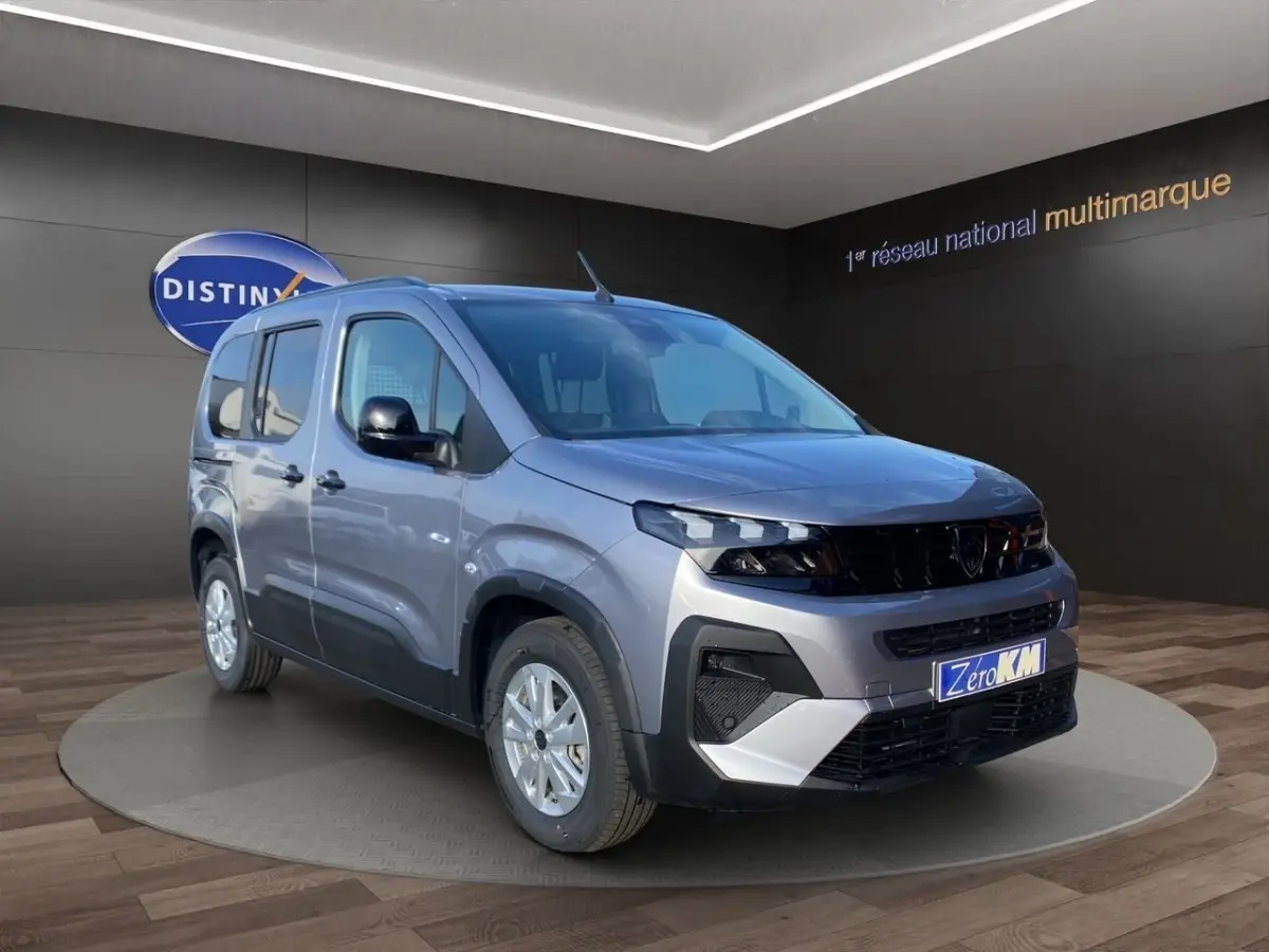 Peugeot Rifter gris clair en 3/4 avant droit, avec calandre noire et jantes argentées, en intérieur showroom.