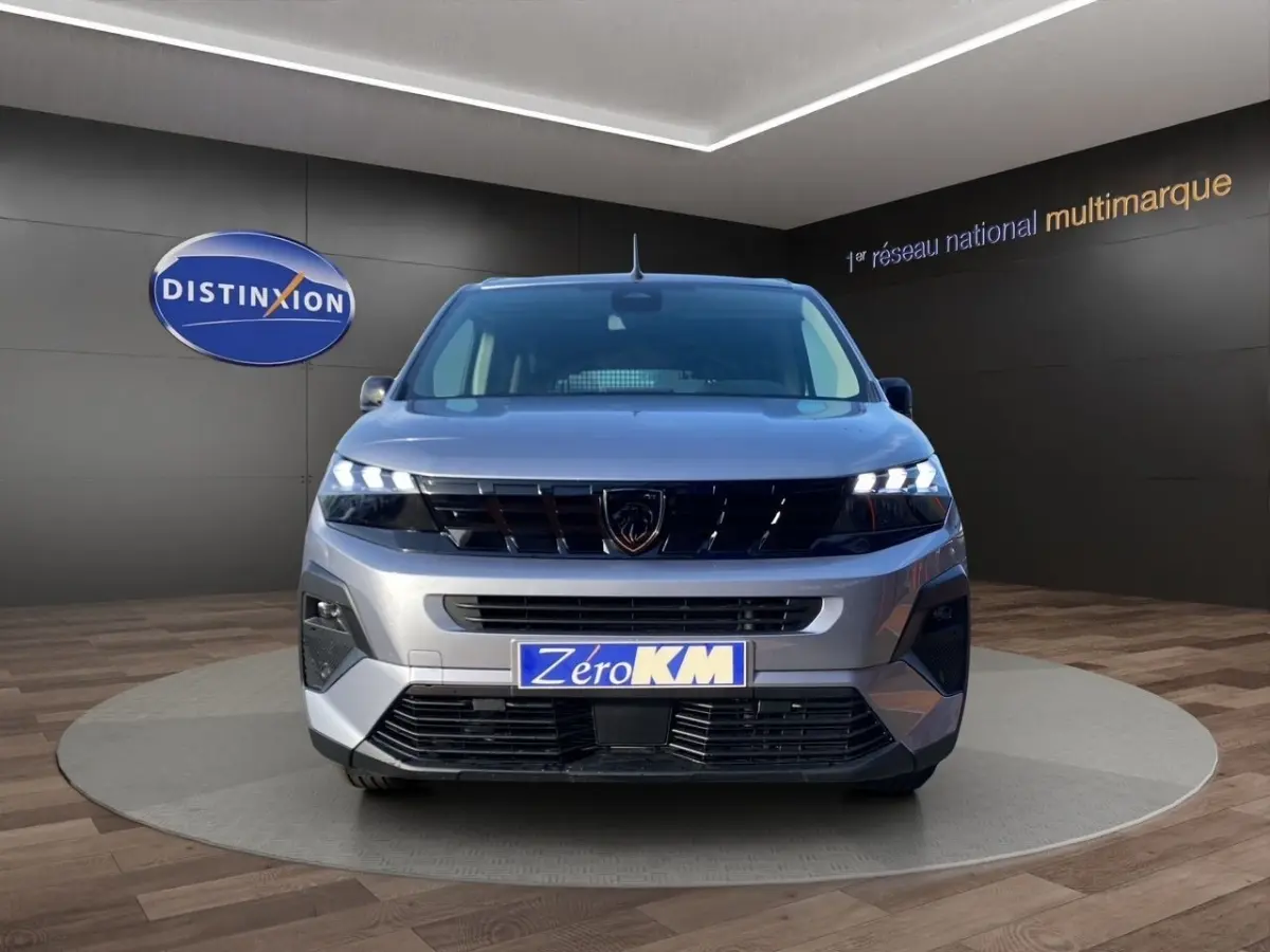 Vue frontale d'un Peugeot Rifter gris clair 2026 avec feux LED allumés et calandre noire brillante.