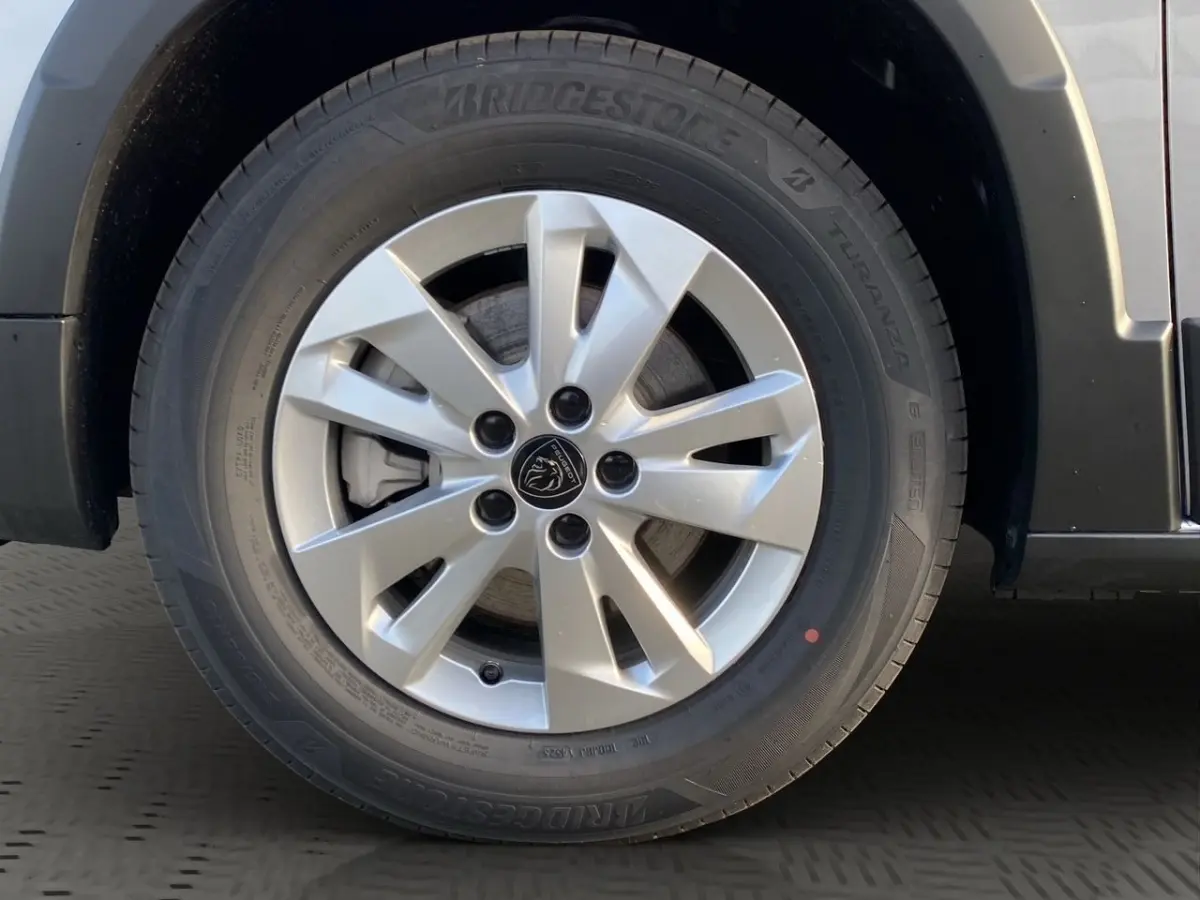 Gros plan sur la roue avant droite du Peugeot Rifter gris clair, jante alliage à 5 doubles branches et logo lion central.