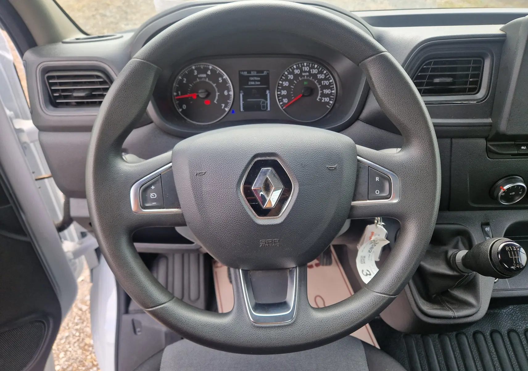 Vue intérieure centrée sur le volant noir Renault d’un Master Châssis Cabine blanc avec tableau de bord et levier de vitesse manuel.