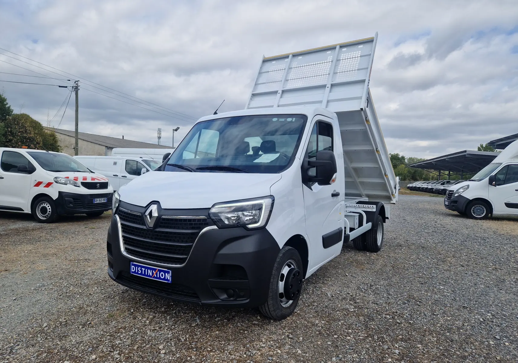 Renault Master Benne blanc vu en 3/4 avant droit, benne relevée et roues jumelées visibles sur terrain gravillonné.