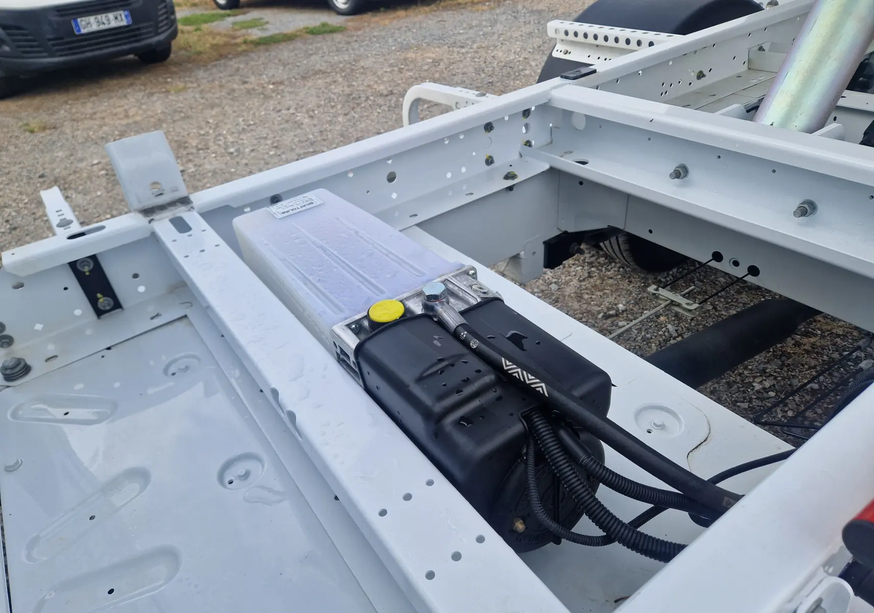 Vue rapprochée du châssis blanc du Renault Master Benne L2 avec composants hydrauliques et roues jumelées visibles.