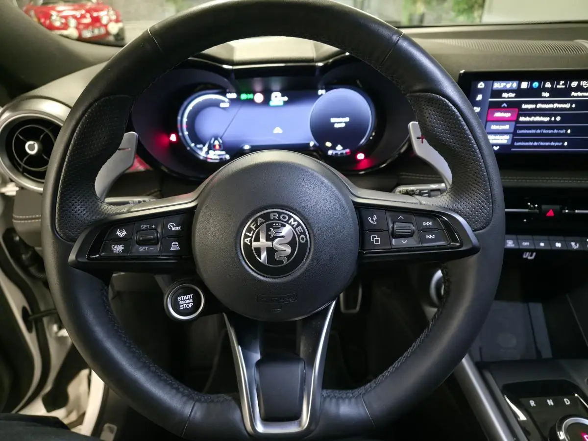 Vue rapprochée du volant en cuir noir perforé de l'Alfa Romeo Tonale 2025 avec tableau de bord digital et écran tactile.