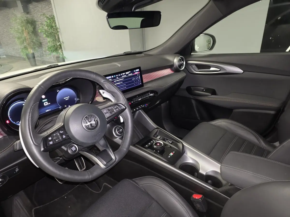 Vue intérieure côté conducteur de l'Alfa Romeo Tonale 2025, volant cuir noir et tableau de bord digital avec inserts rouges.