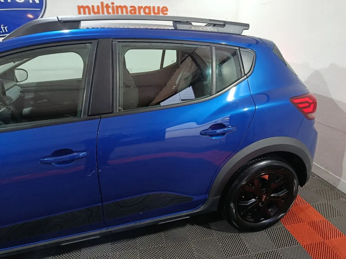 Vue latérale gauche d'une Dacia Sandero Extreme+ TCe 110 2024 bleu avec jantes noires et détails noirs sur les bas de caisse.