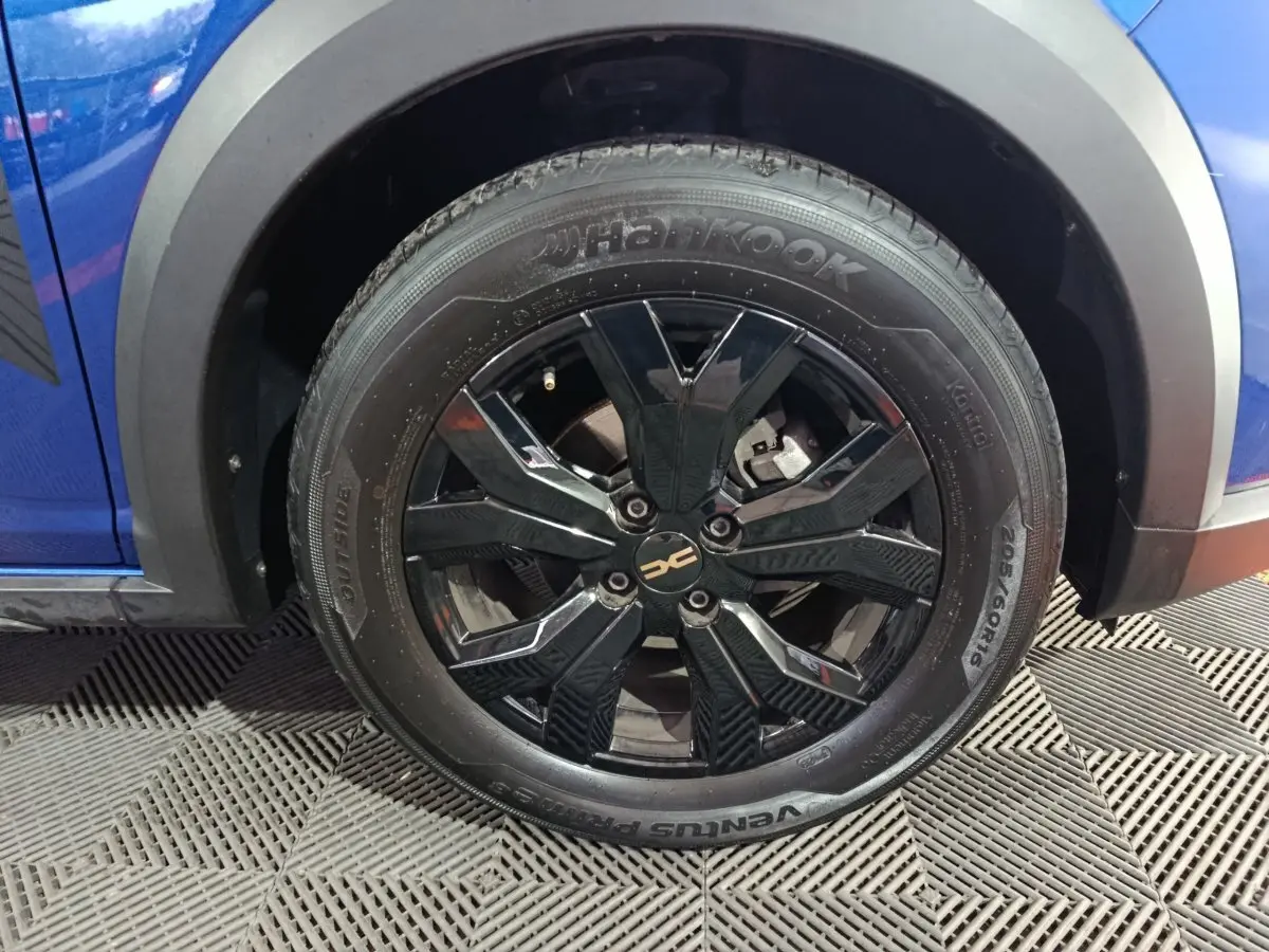Gros plan sur la roue avant gauche noire brillante d'une Dacia Sandero Extreme+ bleu 2024 avec jante en alliage.