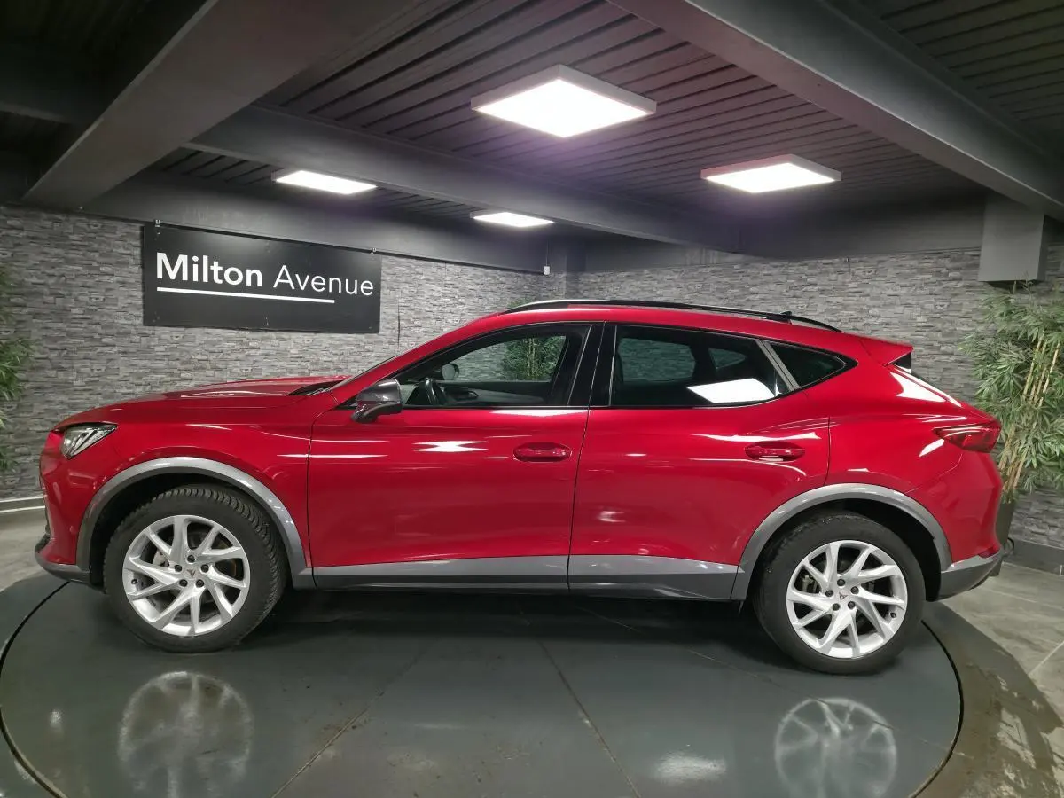 Vue latérale droite d'un CUPRA Formentor rouge avec jantes alliage 18'', entourages d'ailes gris et toit noir en intérieur showroom.