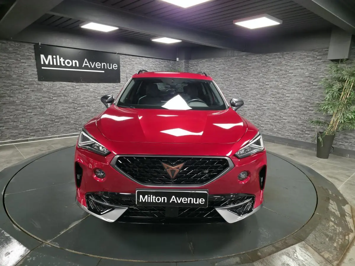 Vue avant d'un CUPRA Formentor rouge avec calandre noire et logo cuivre, dans un showroom au sol circulaire.