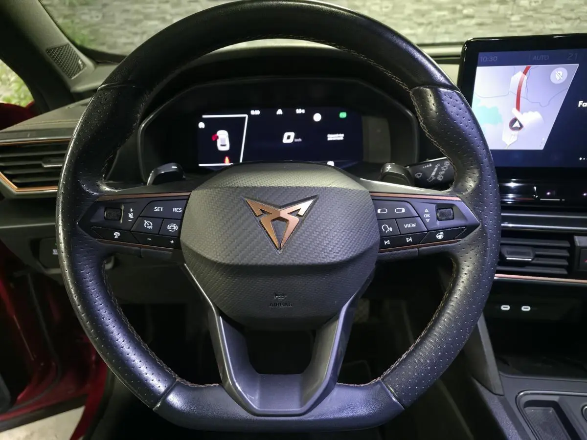 Vue rapprochée du volant cuir perforé noir avec logo CUPRA cuivre et tableau de bord digital du Formentor rouge.
