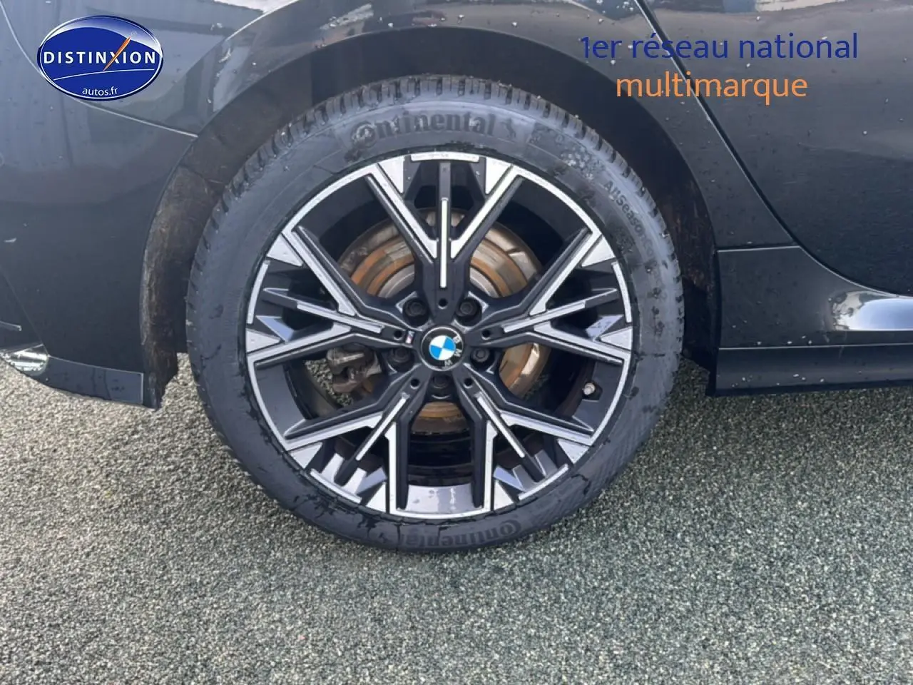 Gros plan sur la roue arrière droite noire d'une BMW Série 1 120da 2024 avec jante alu design sportif.