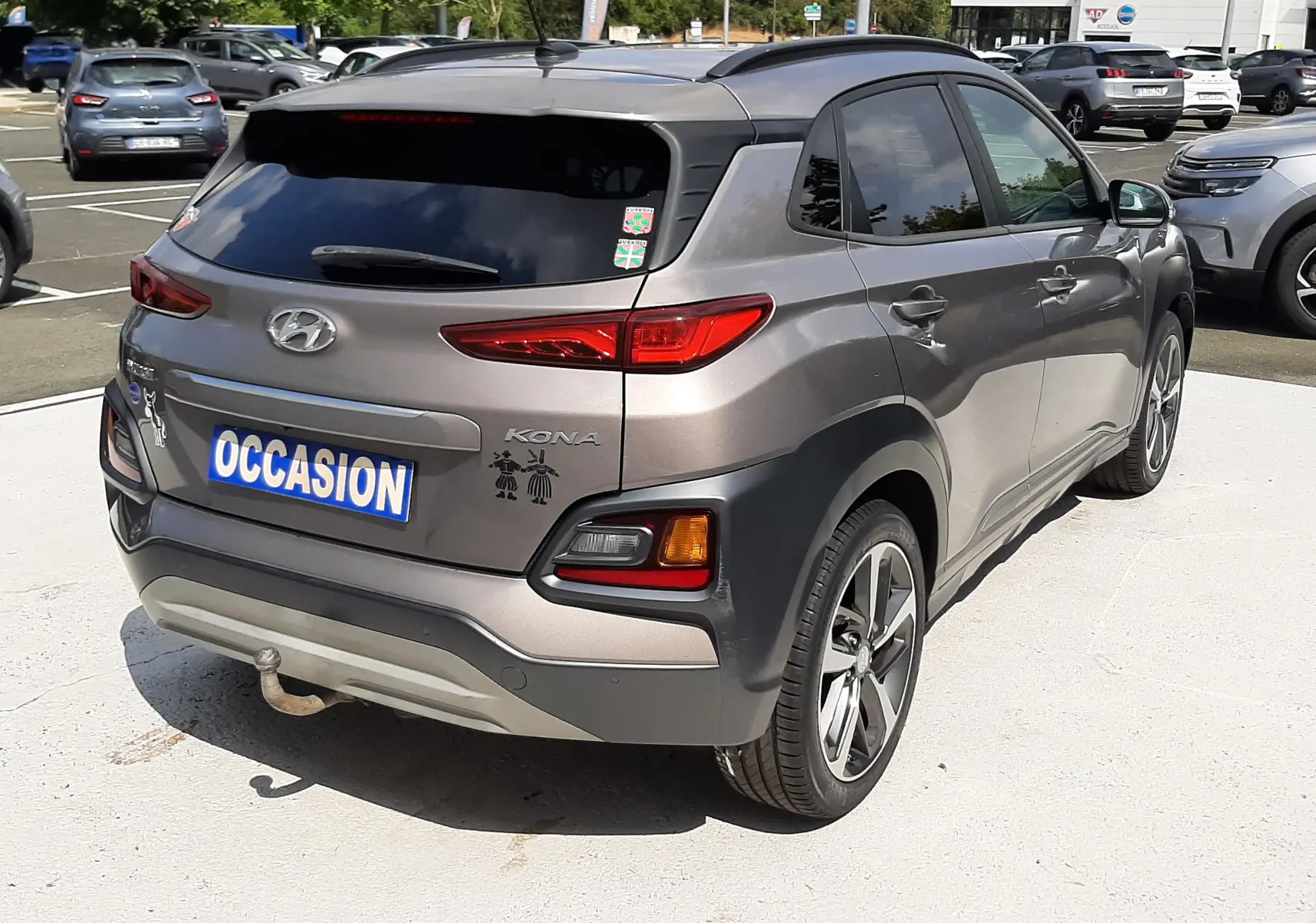 Vue 3/4 arrière droite d'un Hyundai Kona gris 2018 avec stickers décoratifs sur le hayon, stationné en extérieur.