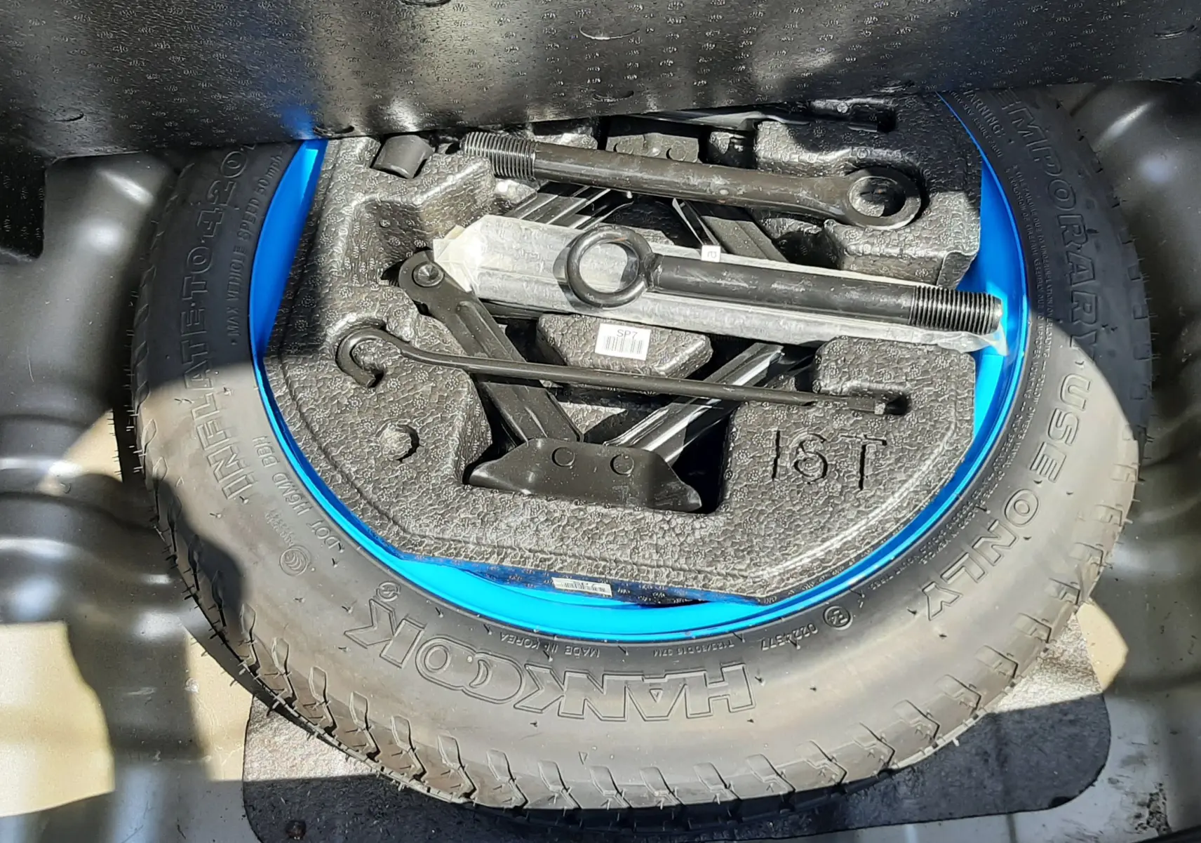 Vue plongeante sur la roue de secours grise et bleue avec outils de changement dans le coffre d'un Hyundai Kona 2018.
