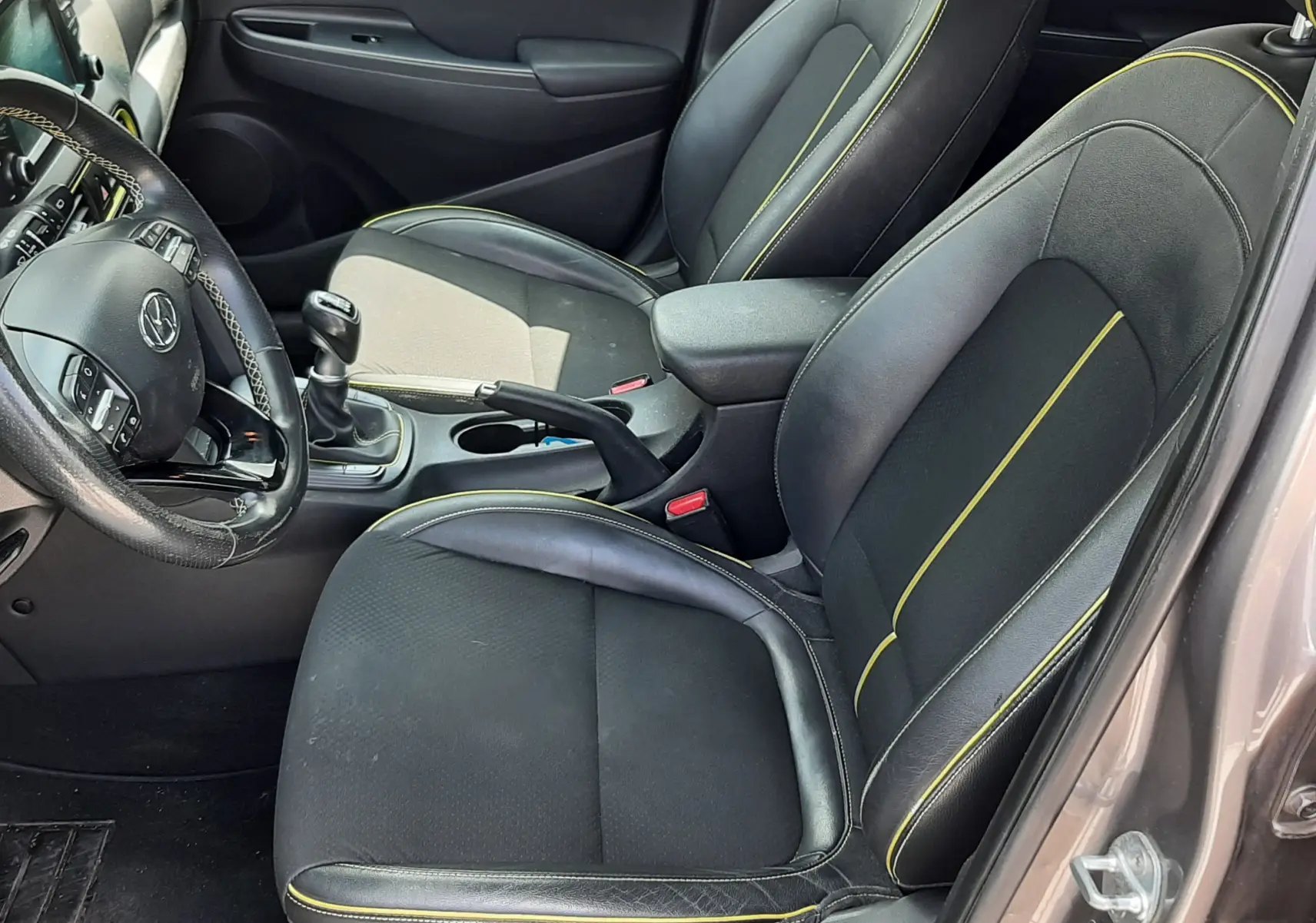 Vue intérieure côté conducteur de la Hyundai Kona 2018, sièges noirs avec surpiqûres jaunes et volant multifonction.