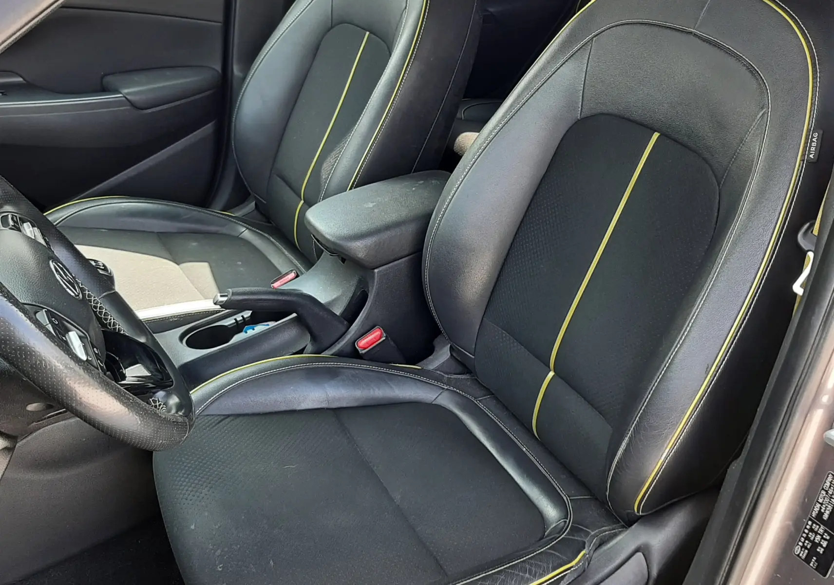 Vue intérieure côté conducteur du Hyundai Kona 2018, sièges noirs avec surpiqûres jaunes et volant partiellement visible.