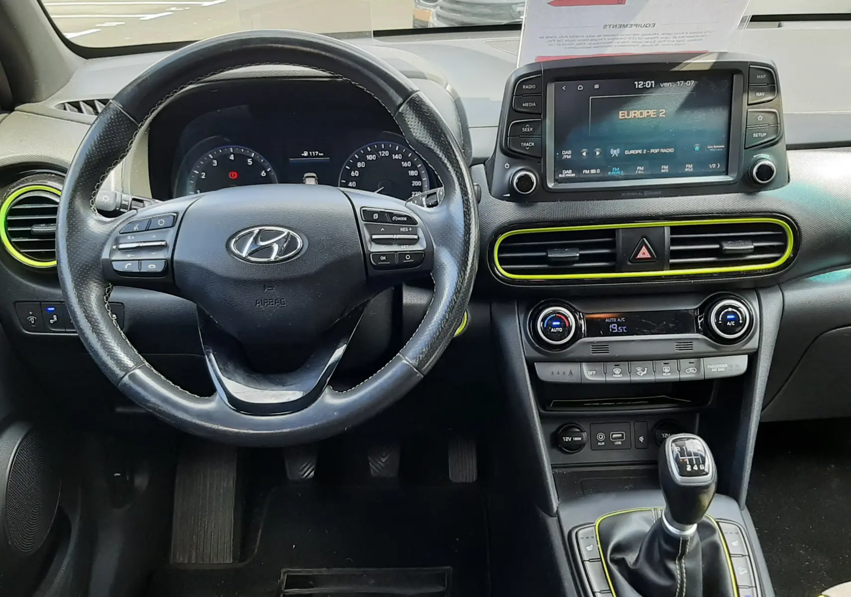 Vue intérieure avant du Hyundai Kona gris 2018, volant multifonction, écran tactile, et levier de vitesse manuel avec surpiqûres jaunes.
