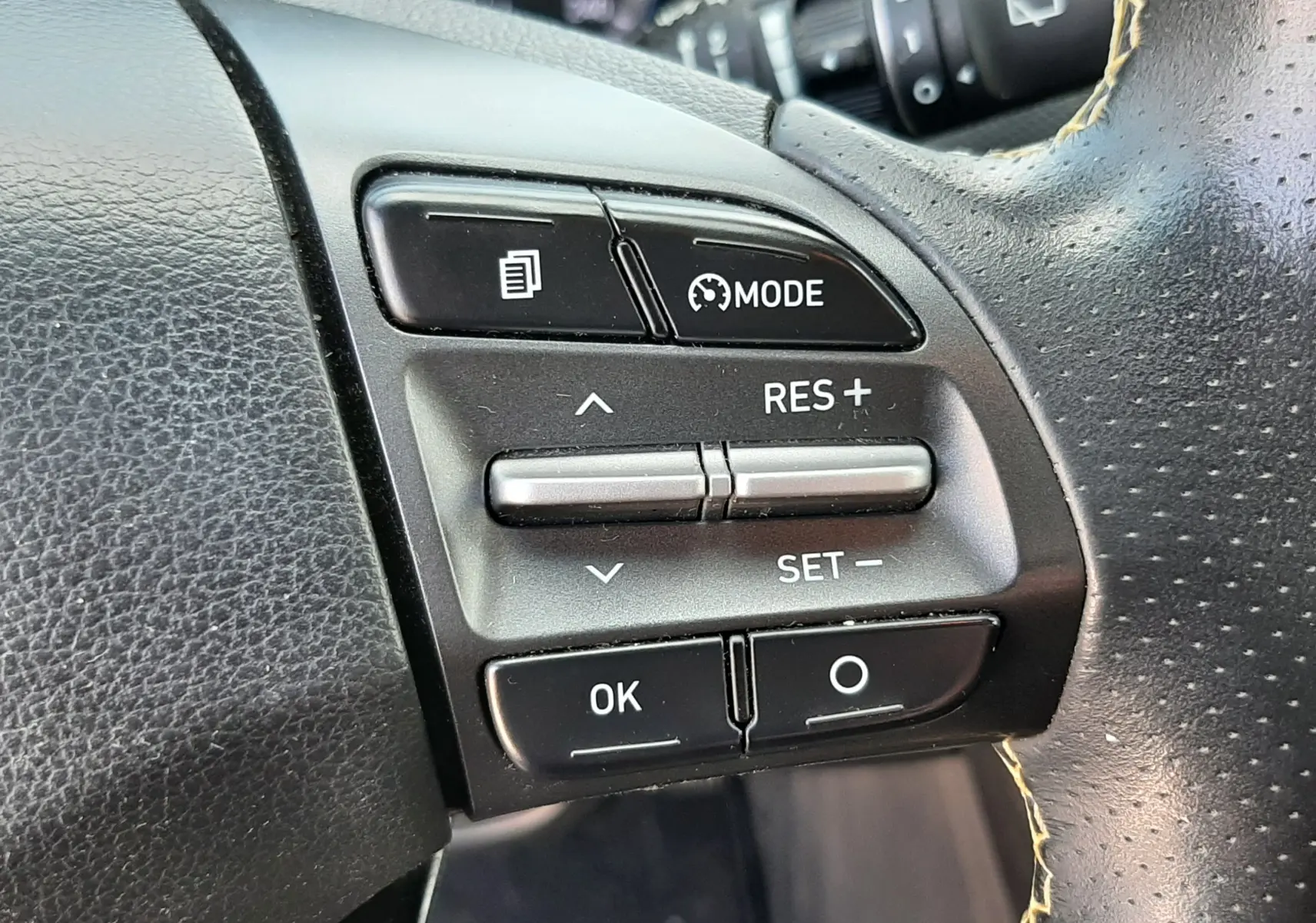 Gros plan sur les commandes au volant côté droit du Hyundai Kona gris, avec boutons de régulateur de vitesse et mode.