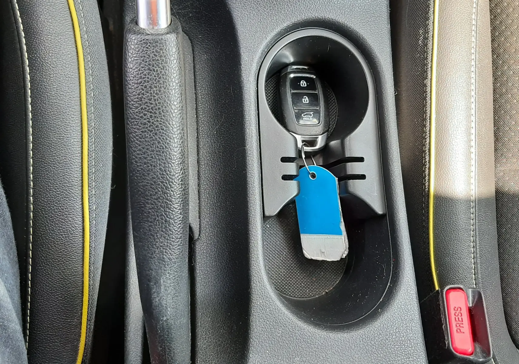 Vue rapprochée de la console centrale noire avec frein à main, porte-clés Hyundai et surpiqûres jaunes des sièges gris.