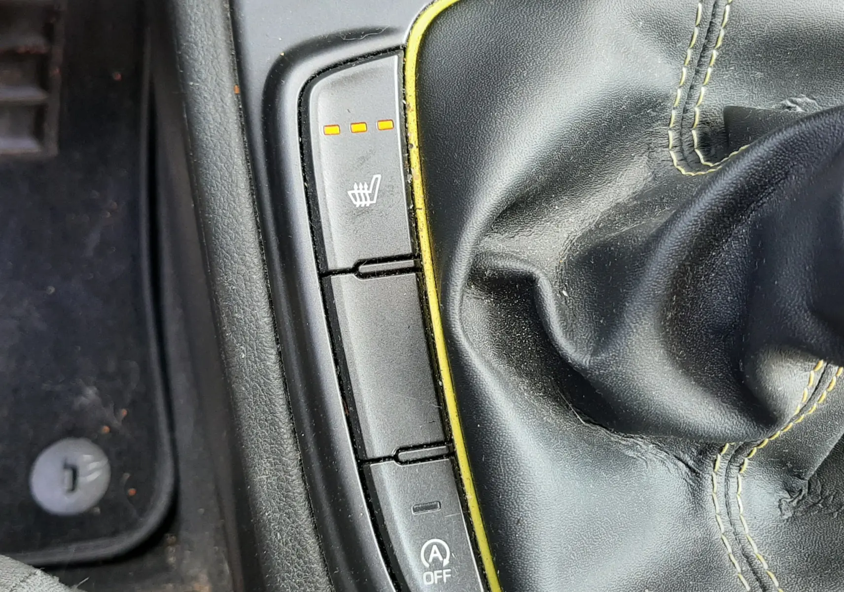 Gros plan sur la commande de siège chauffant et levier de vitesse en cuir noir avec surpiqûres jaunes dans Hyundai Kona gris.