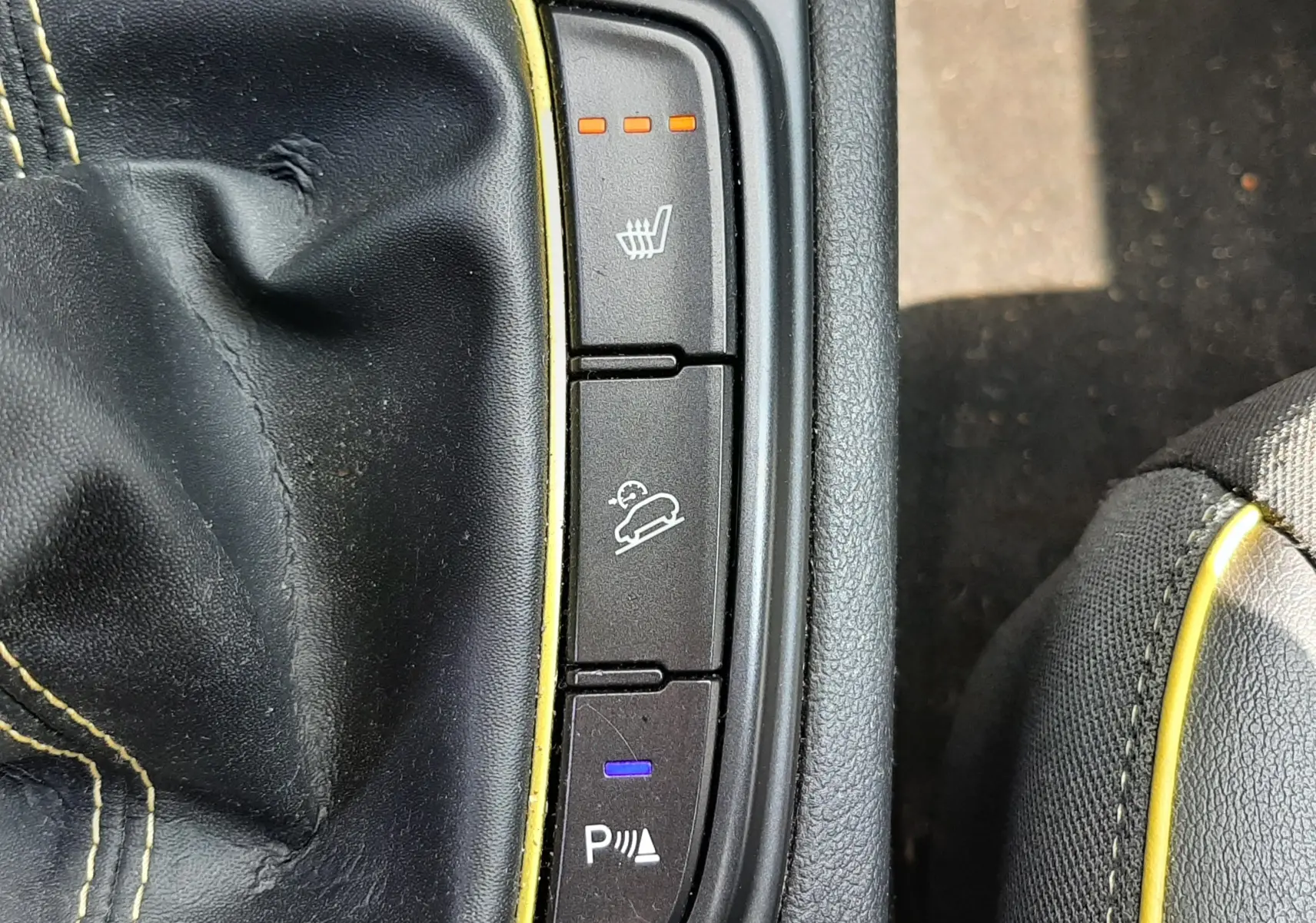 Vue rapprochée sur la console centrale d'une Hyundai Kona gris, montrant les boutons de siège chauffant, aide à la descente et capteurs de stationnement.