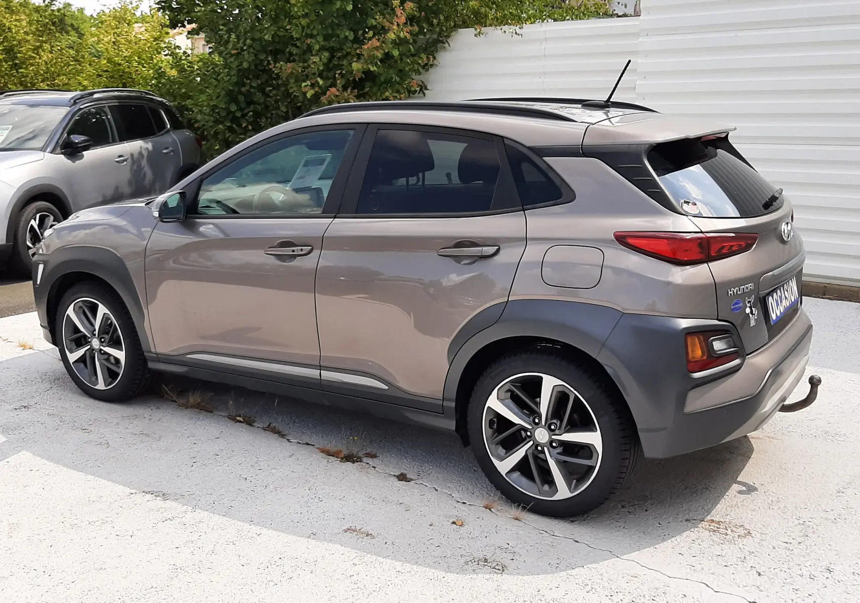 Hyundai Kona gris en vue 3/4 arrière droit, avec jantes alliage et toit ouvrant visible, stationné sur parking extérieur.