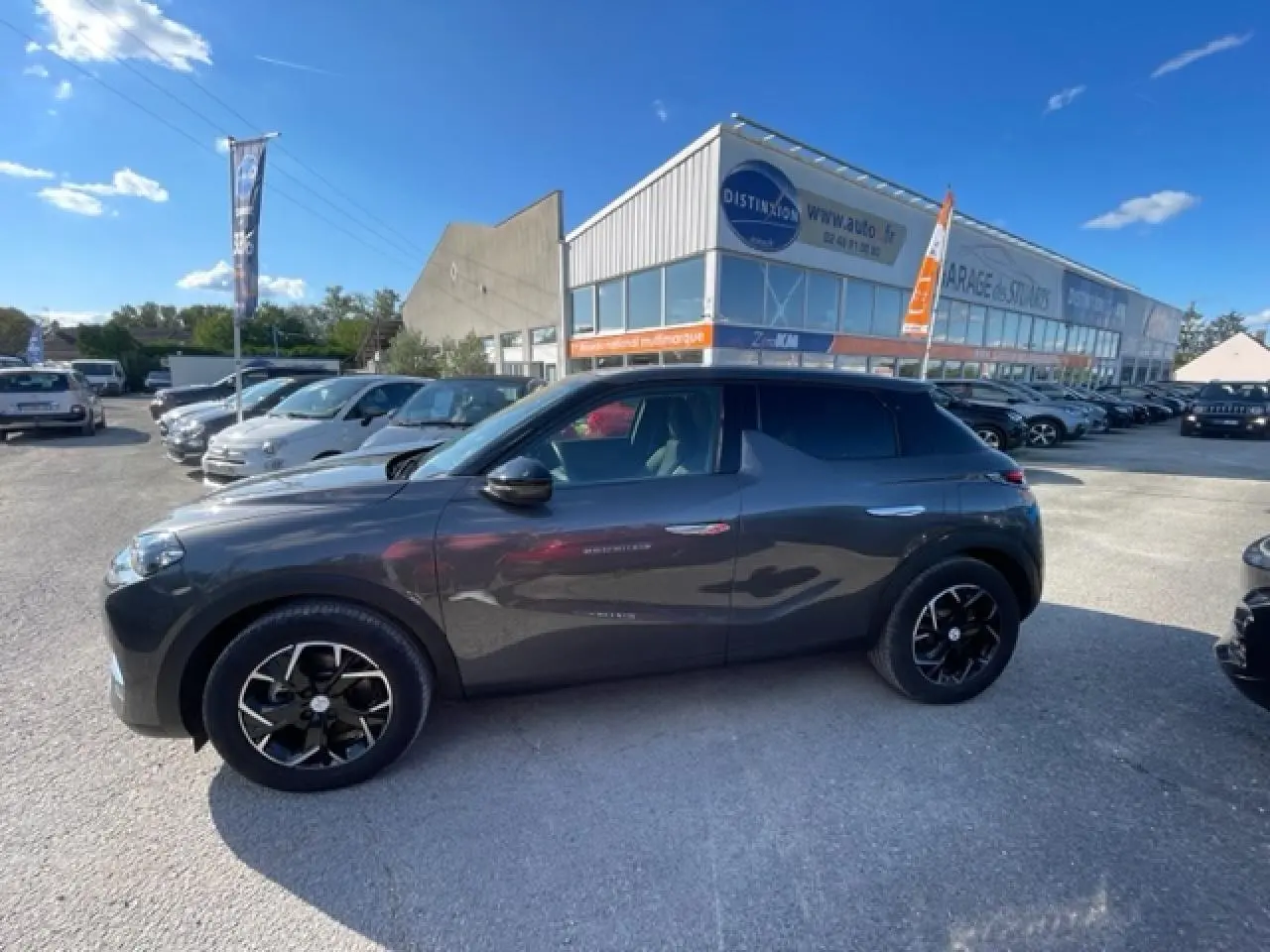 Vue de profil côté gauche d’un DS3 Crossback E-Tense gris platinium avec jantes noires et toit noir, stationné en extérieur.