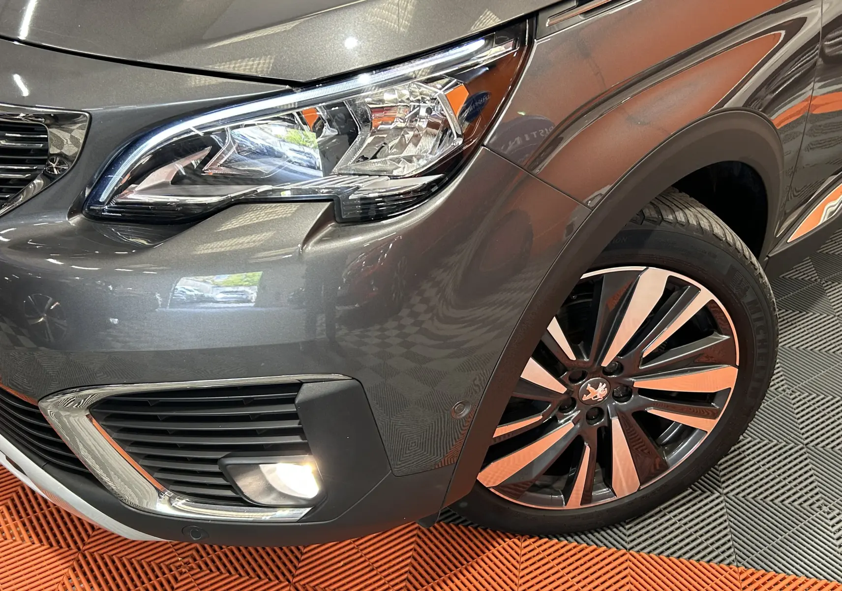 Gros plan sur l'avant droit gris du Peugeot 5008 2020, mettant en valeur le phare LED et la jante alliage bicolore.