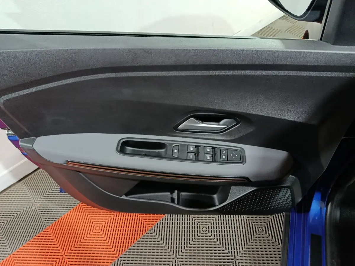 Vue intérieure côté gauche de la porte avant bleue d’une Dacia Sandero Extreme+ avec commandes électriques et poignée grise.