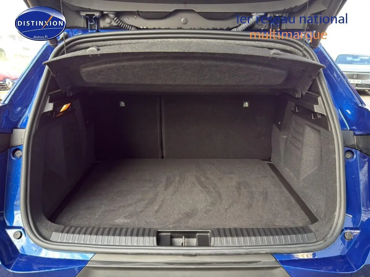 Coffre ouvert vu de l'arrière d'une Renault Symbioz bleu iron metal, espace de chargement vide et tapis gris.