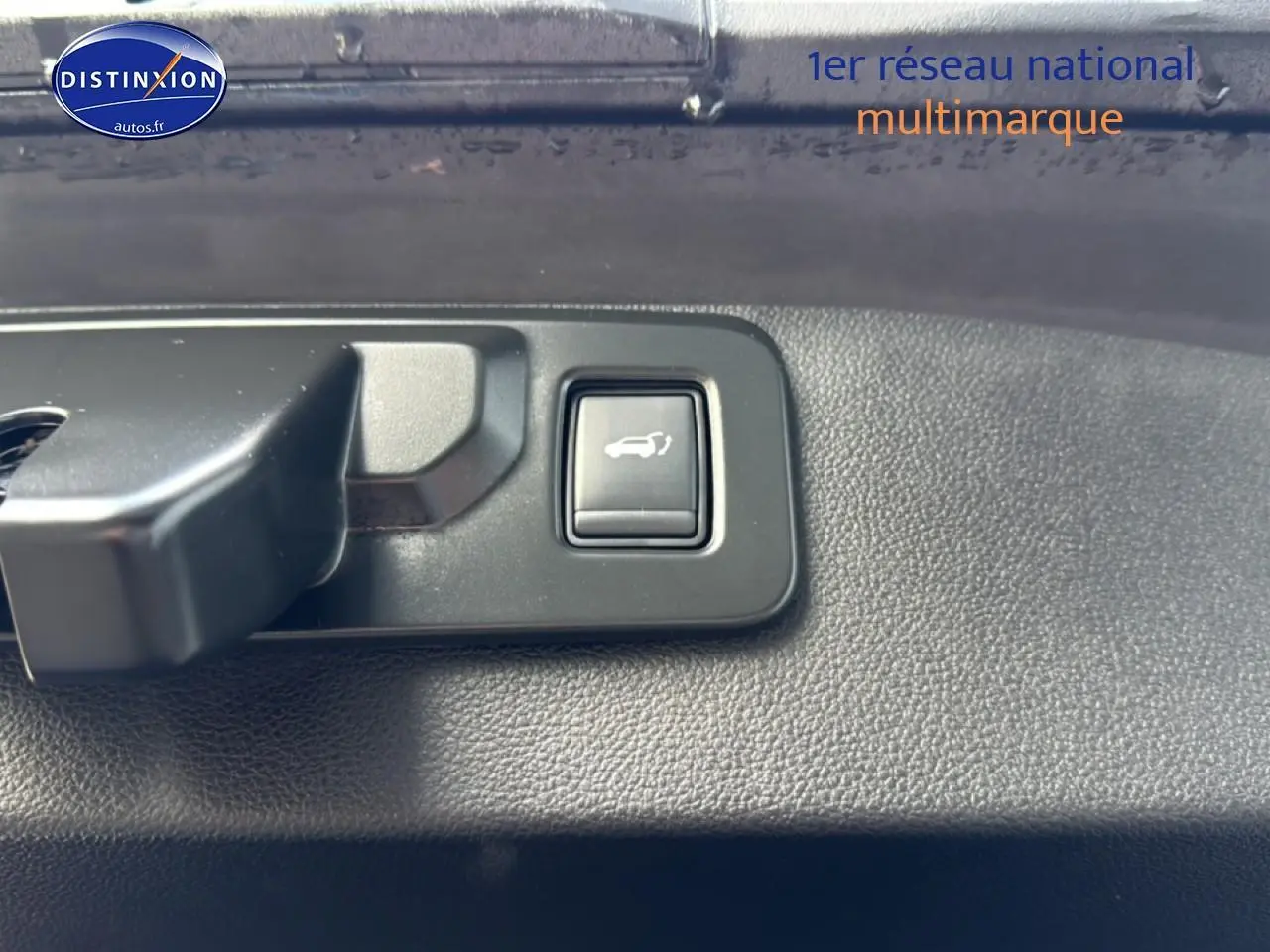 Bouton d'ouverture du coffre en gros plan sur panneau intérieur noir du Renault Symbioz bleu iron metal.