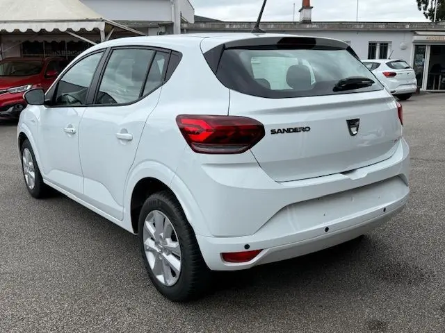 Vue 3/4 arrière droite d'une Dacia Sandero blanc glacier 2023, avec feux arrière rouges et logo SANDERO visible.