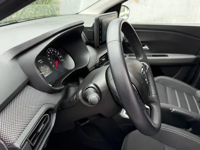 Vue intérieure côté conducteur du Dacia Sandero blanc glacier 2023, tableau de bord et volant en cuir visibles.