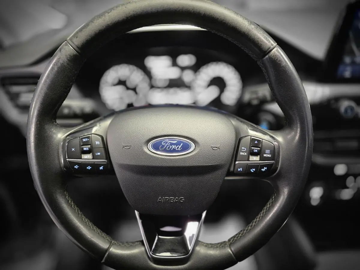 Vue rapprochée du volant noir du Ford Kuga 1.5 EcoBlue 2020 avec commandes intégrées et logo Ford central.