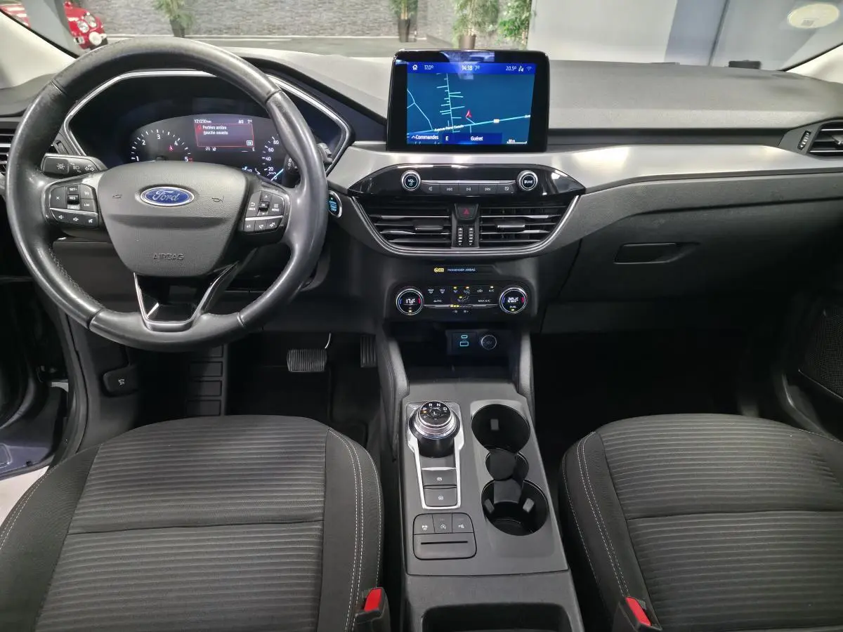 Vue intérieure avant du Ford Kuga 2020 gris, avec volant multifonction, écran tactile central et console avec sélecteur rotatif.