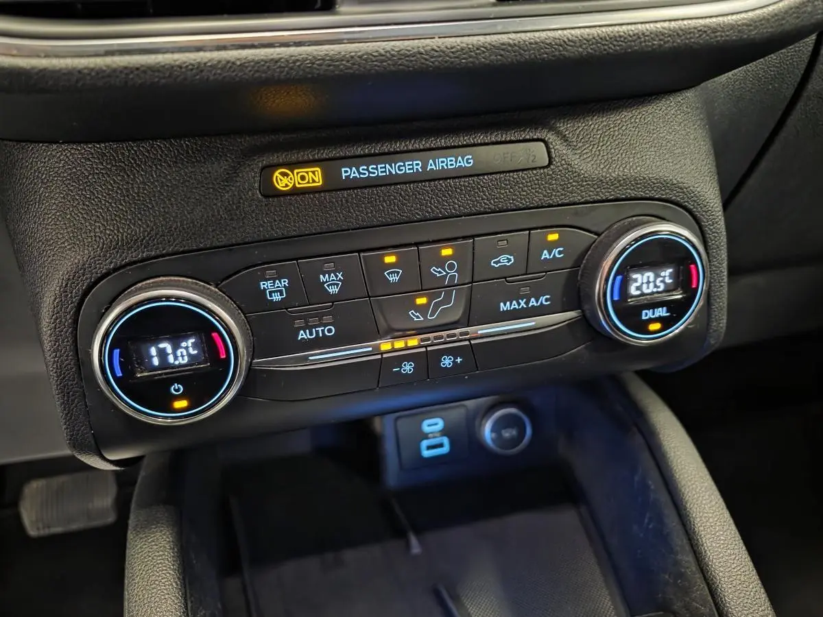 Gros plan sur la console centrale noire du Ford Kuga 2020, affichant la climatisation automatique bi-zone et l'indicateur airbag passager.