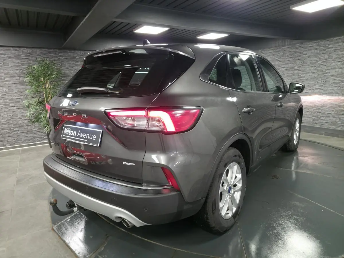 Vue 3/4 arrière droite d'un Ford Kuga gris métallisé 2020 avec attelage fixe et feux arrière LED allumés.