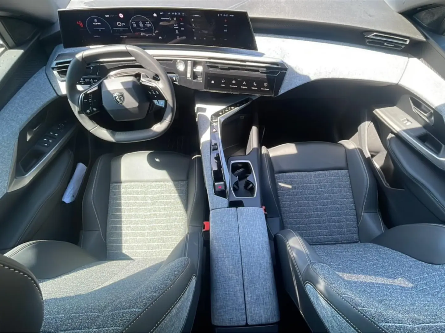 Vue intérieure de face du Peugeot 3008 2025, sièges tissu gris et cuir noir, tableau de bord numérique et console centrale moderne.