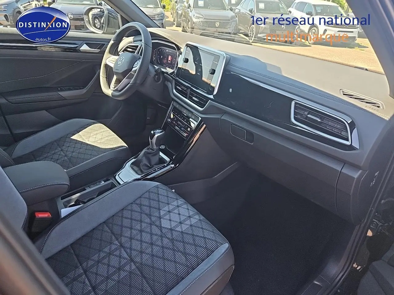 Intérieur du Volkswagen T-Roc 2025 vu côté passager, sièges tissu noir à motifs et tableau de bord moderne.