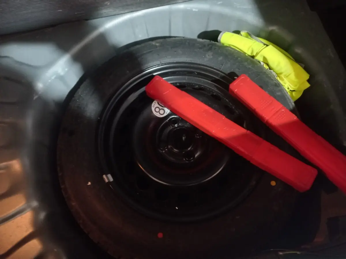 Gros plan sur la roue de secours galette noire dans le coffre d'une Dacia Sandero 2024 avec deux triangles de signalisation rouges.