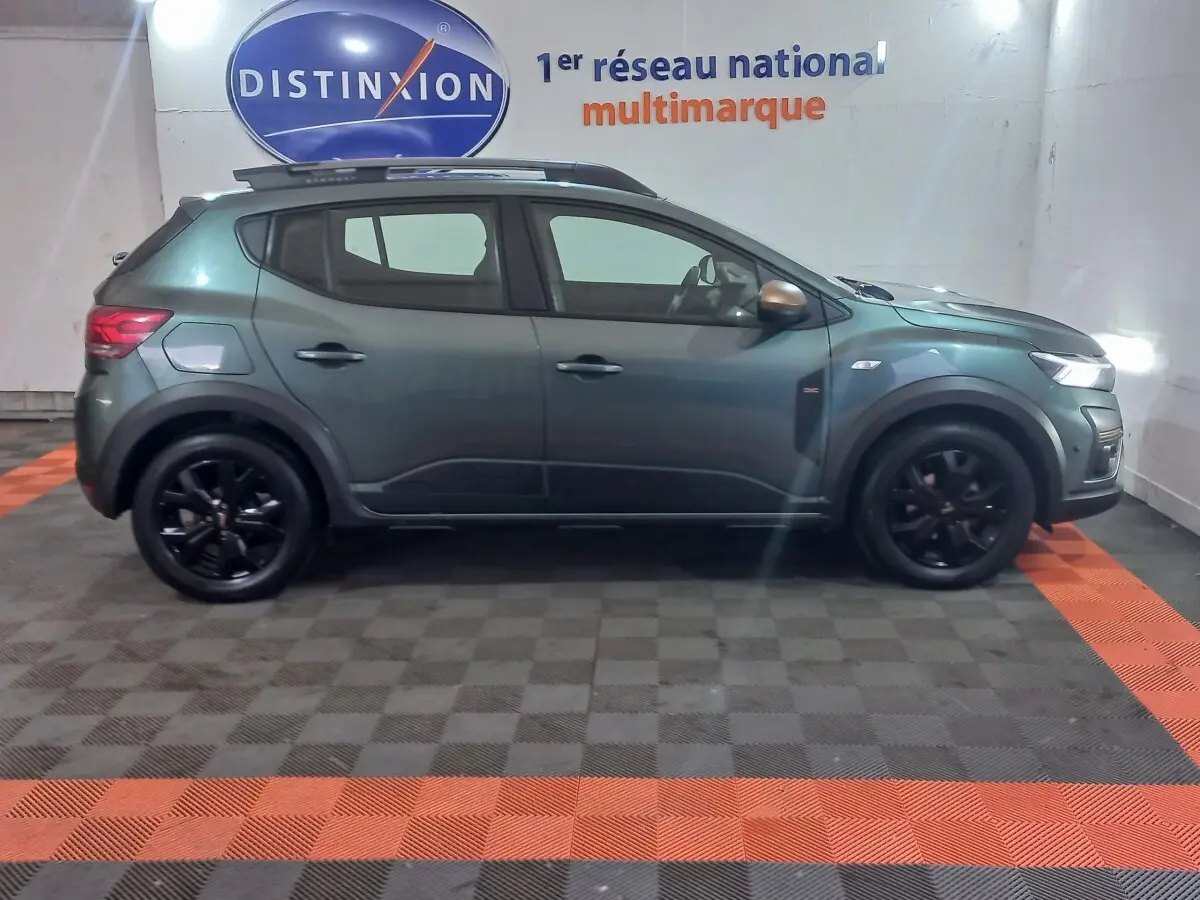 Vue de profil gauche d'une Dacia Sandero Extreme+ TCe 110 2024 vert métallisé avec jantes noires et barres de toit.