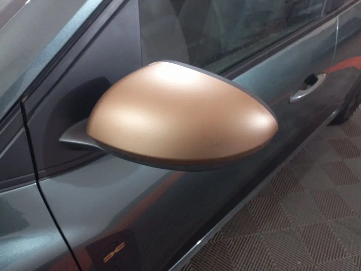 Gros plan sur le rétroviseur droit doré d'une Dacia Sandero 2024 vert foncé, avec poignée de porte visible.