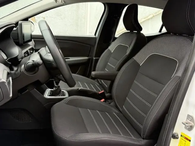 Vue intérieure côté conducteur de la Dacia Sandero 2023 blanc glacier, montrant les sièges noirs avec surpiqûres blanches et la boîte manuelle.