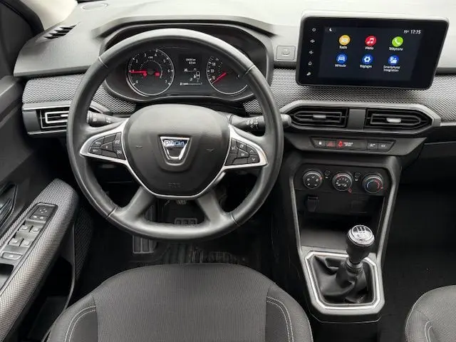 Vue intérieure du tableau de bord de la Dacia Sandero 2023, volant multifonction, écran tactile et levier de vitesse manuel.
