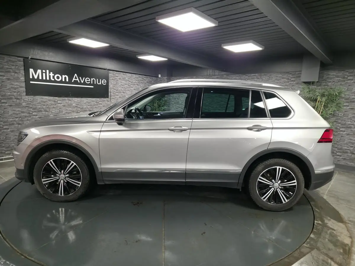 Volkswagen Tiguan gris en profil droit, avec jantes alliage noires et chrome, dans un showroom intérieur.