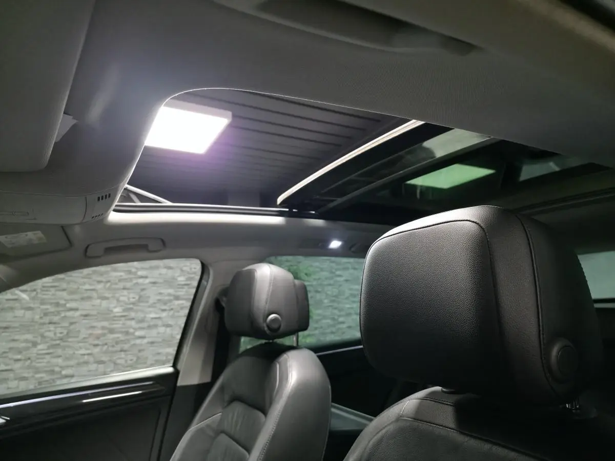 Intérieur du Volkswagen Tiguan 2016, vue sur les sièges avant en cuir noir et toit ouvrant panoramique ouvert.