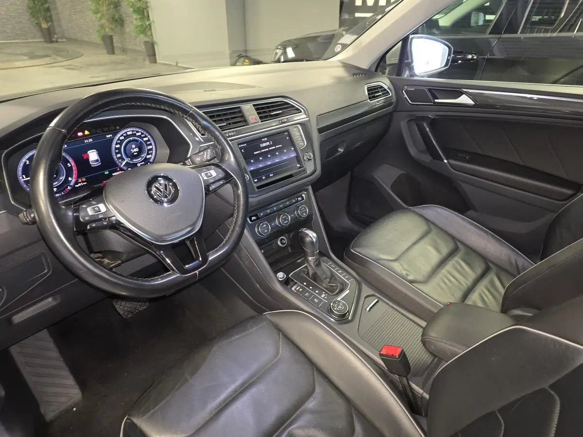 Vue intérieure du Volkswagen Tiguan 2016 côté conducteur, avec tableau de bord numérique et sièges sport cuir noirs.