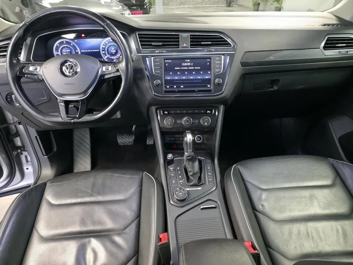 Vue intérieure avant du Volkswagen Tiguan 2016 avec tableau de bord noir, volant cuir multifonctions et console centrale avec écran tactile.