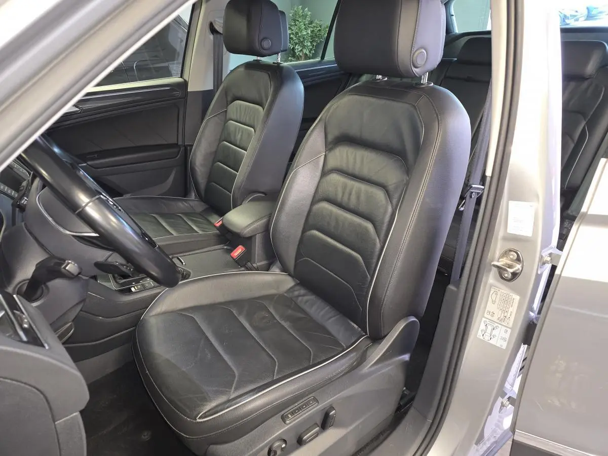 Vue intérieure côté conducteur du Volkswagen Tiguan gris 2016, sièges sport en cuir noir avec réglages électriques.